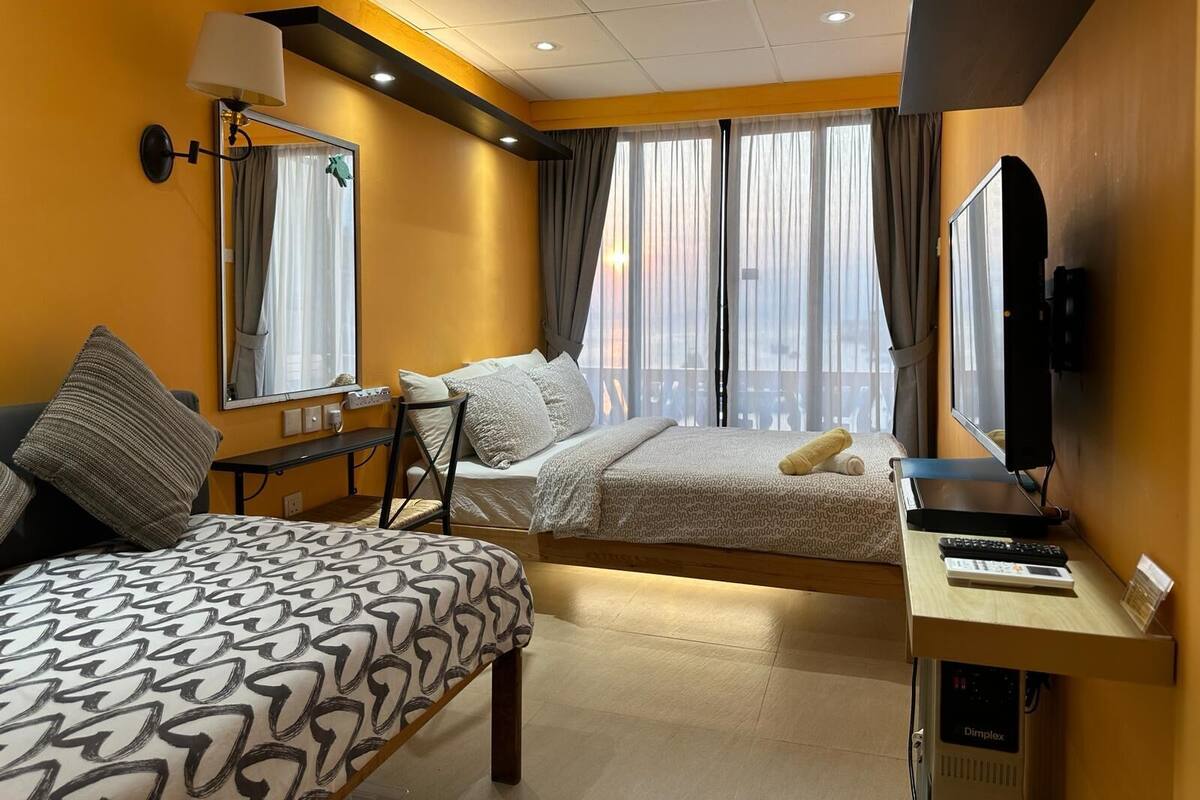 Habitación de hotel con dos camas, un escritorio, un televisor y un ventanal con cortinas.