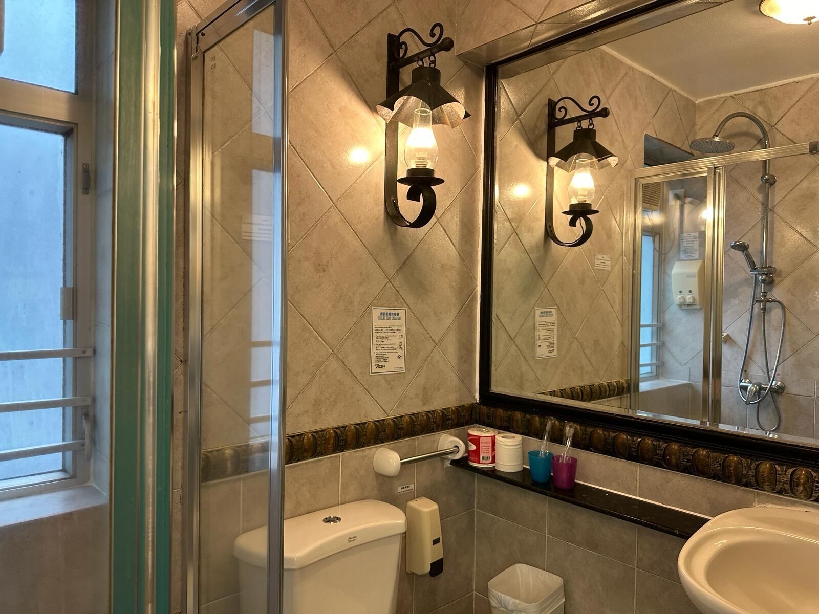 A bathroom with a toilet, sink, and shower. There are wall-mounted lights and a large mirror.