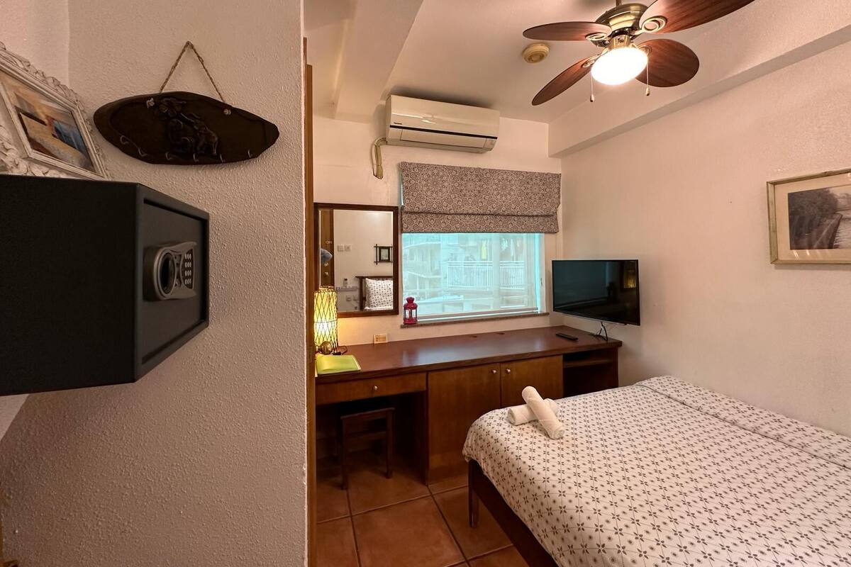 Un dormitorio con cama, escritorio, televisión, ventilador de techo y aire acondicionado.