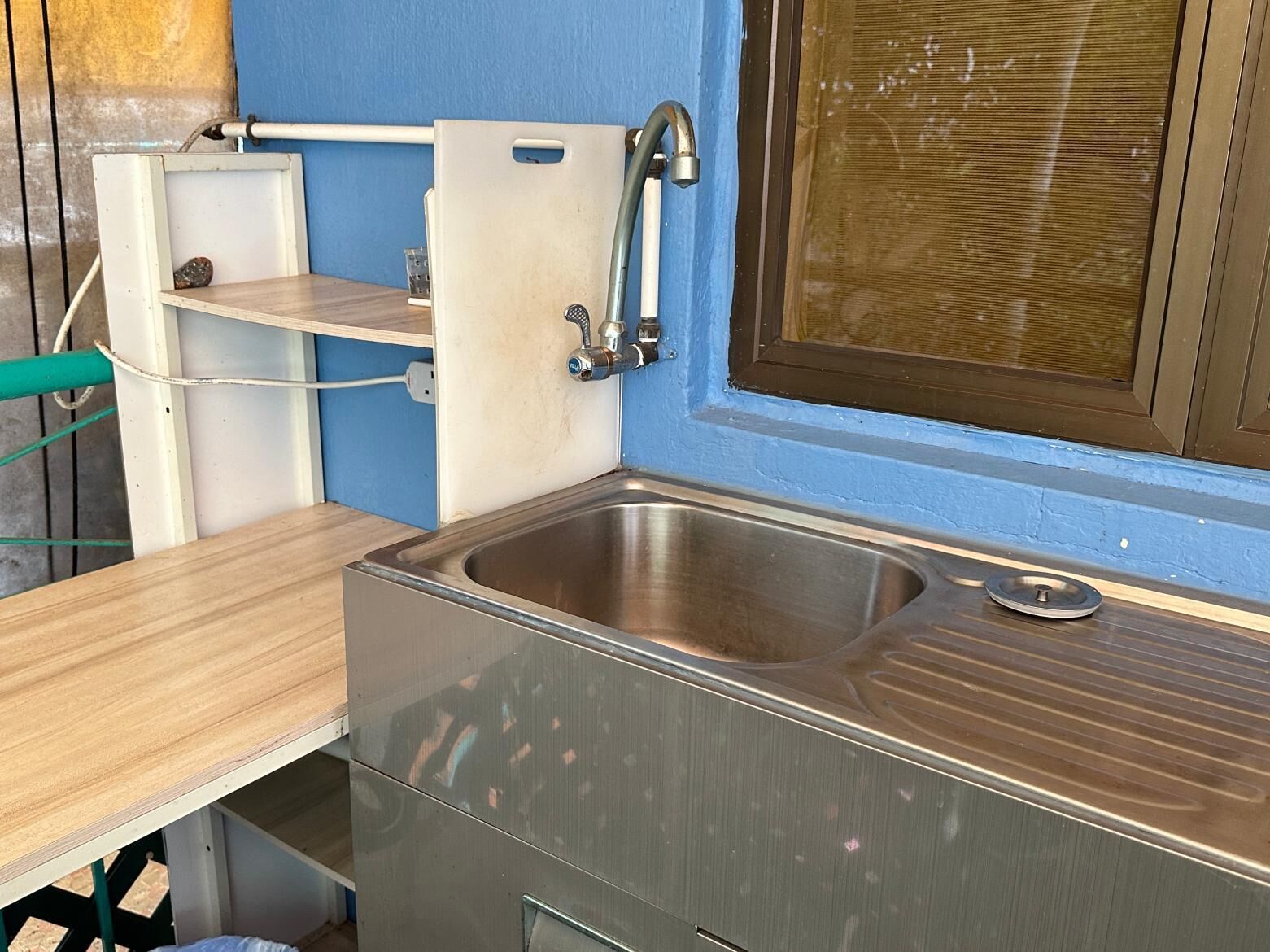 A compact kitchen with a stainless steel sink, a small countertop, and a window with a brown frame.