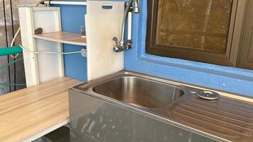 A compact kitchen with a stainless steel sink, a small countertop, and a window with a brown frame.