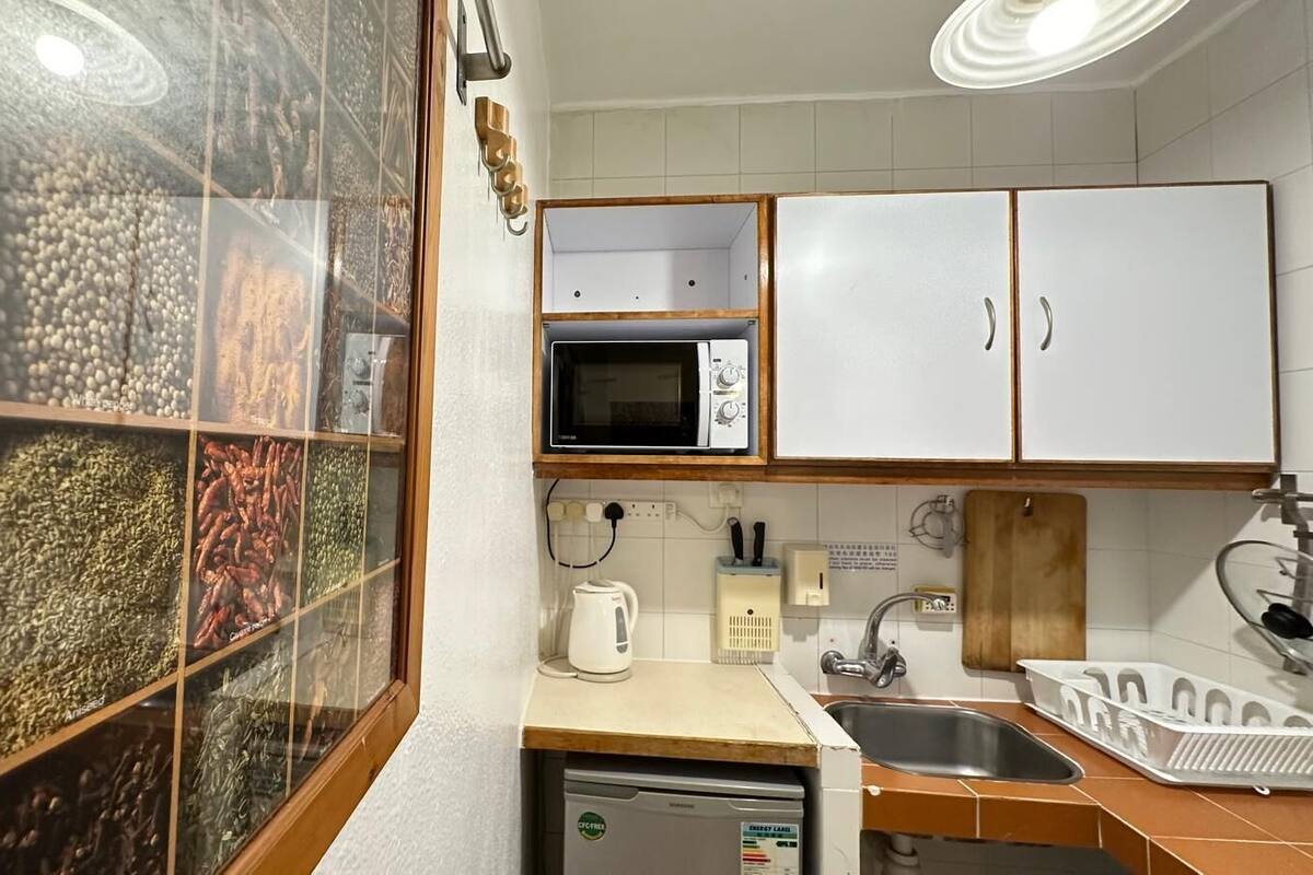 Cocina compacta con microondas, lavabo y un mueble con vitrina de cristal que contiene diversos objetos.