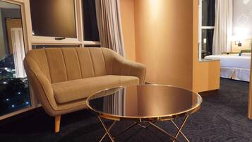 A hotel room with a sofa, a glass-top table, a bed, and a view of the city at night.