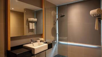 Une salle de bain moderne avec une douche à parois de verre, un lavabo doté d’un plan de travail noir et un miroir au-dessus du lavabo.