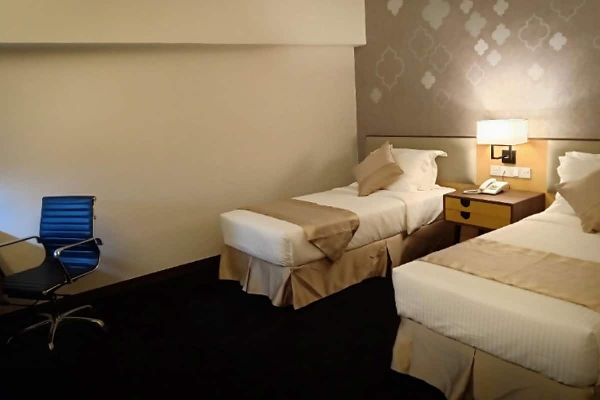 A hotel room with two beds, a desk, a chair, and a lamp.
