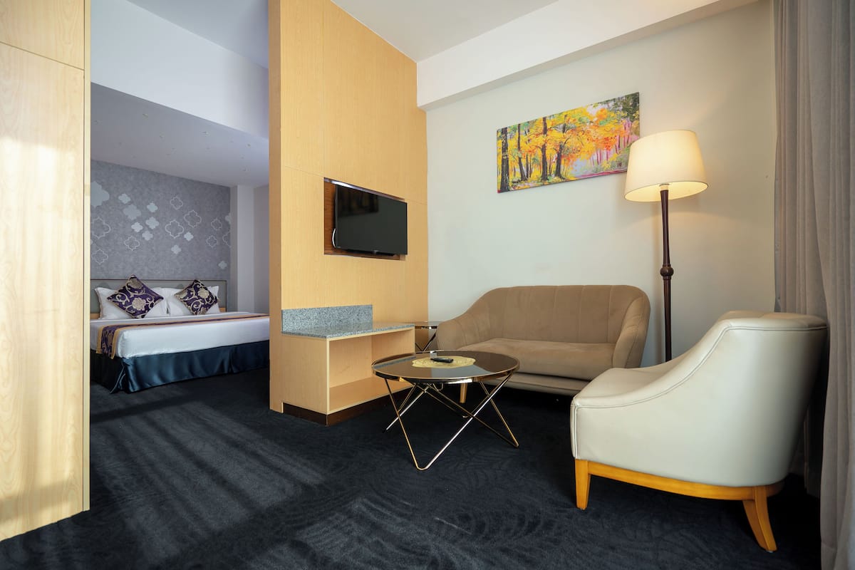 A hotel room with a bed, a sofa, a small table, a TV, and a painting on the wall.