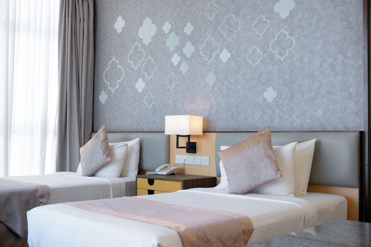 A hotel room with two beds, a nightstand with a lamp, and a patterned wall.