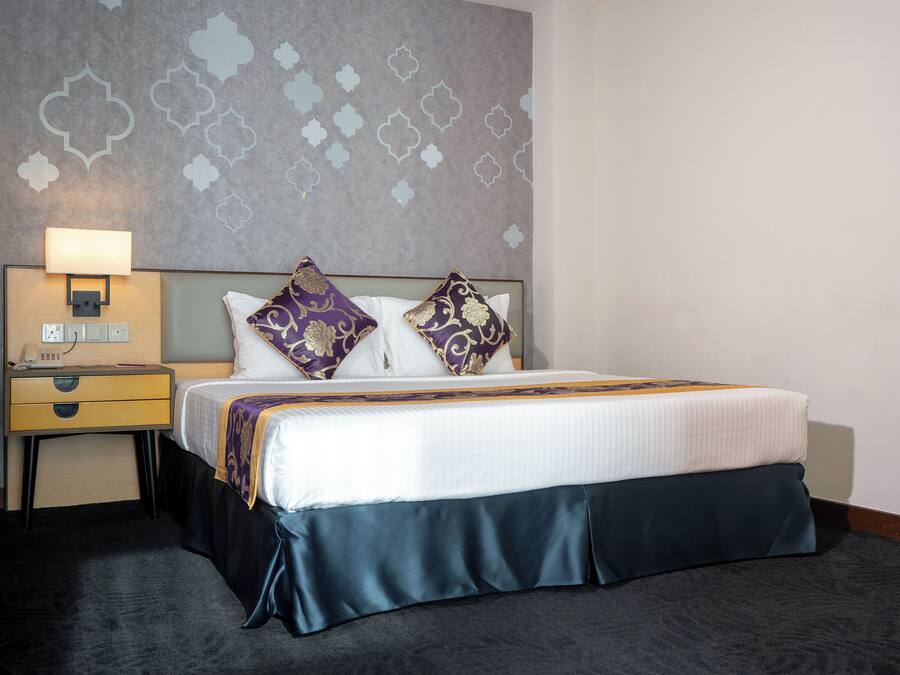A hotel room with a bed, nightstand, lamp, and patterned wall.