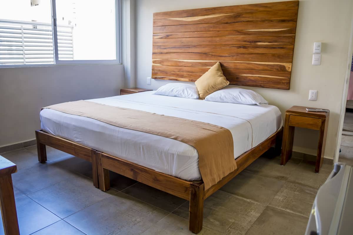 Une chambre à coucher avec un lit en bois, une tête de lit, une table de chevet et une fenêtre avec des stores.