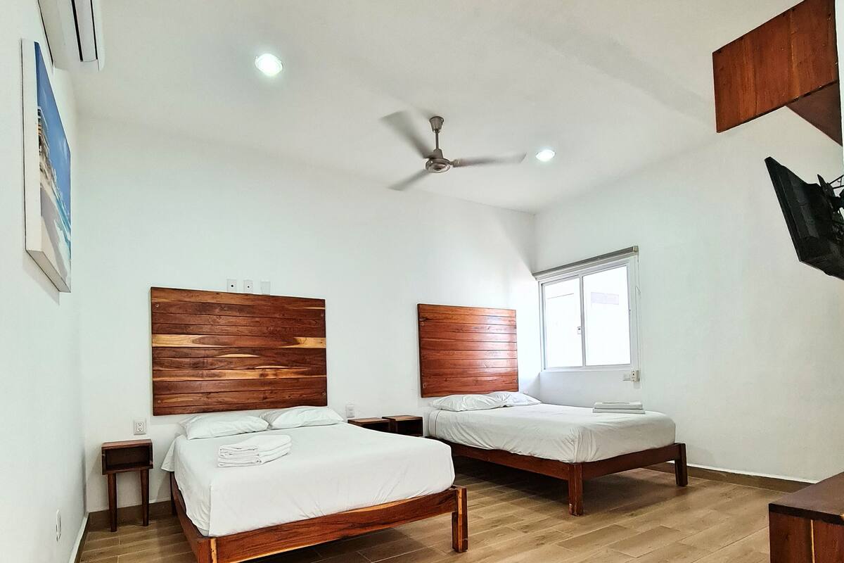 Une chambre avec deux lits en bois, un ventilateur de plafond et une fenêtre.