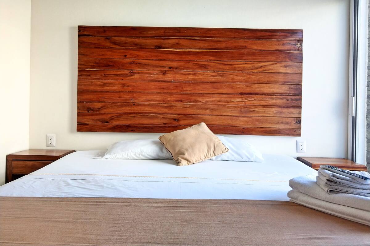 Un lit bien fait, avec une tête de lit en bois, un oreiller beige et une pile de serviettes sur le côté.