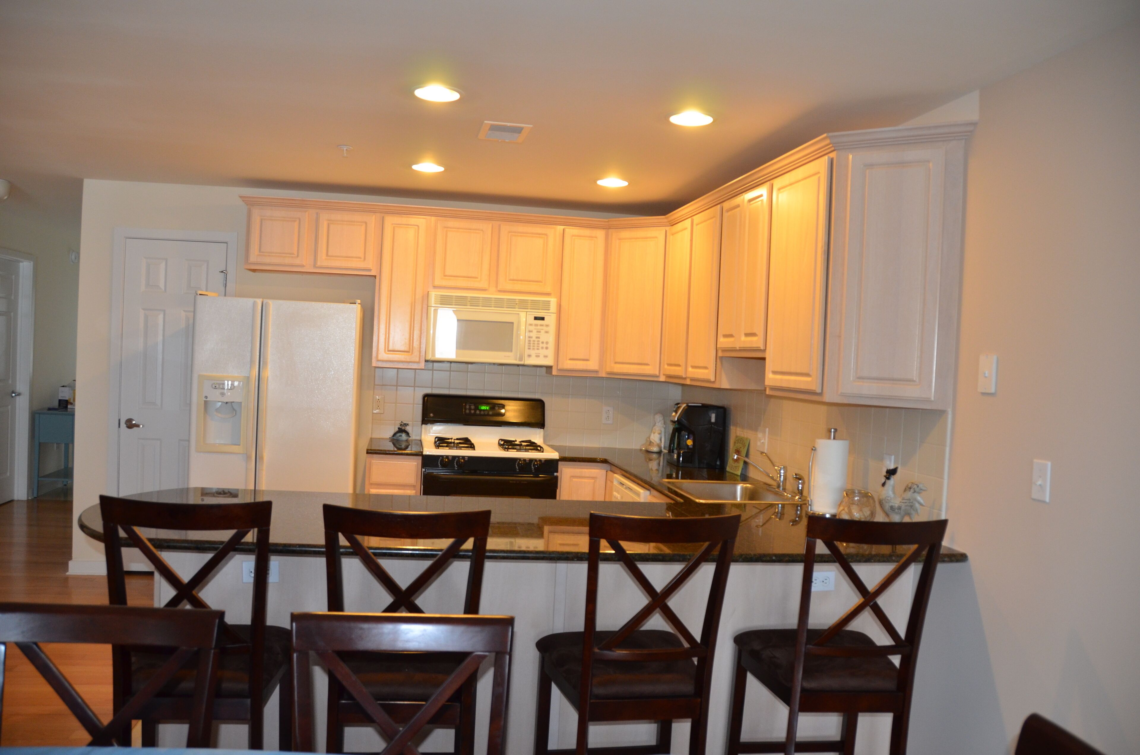 A kitchen with wooden cabinets, a microwave, stove, and a dining area with four chairs.