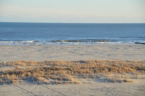 A beach with sand and sparse grass in the foreground, leading to the ocean.