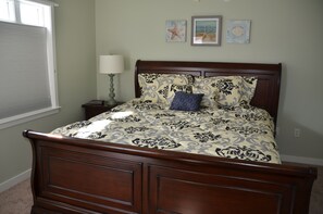 Een slaapkamer met een houten bed, nachtkastje, lamp en wanddecoratie.