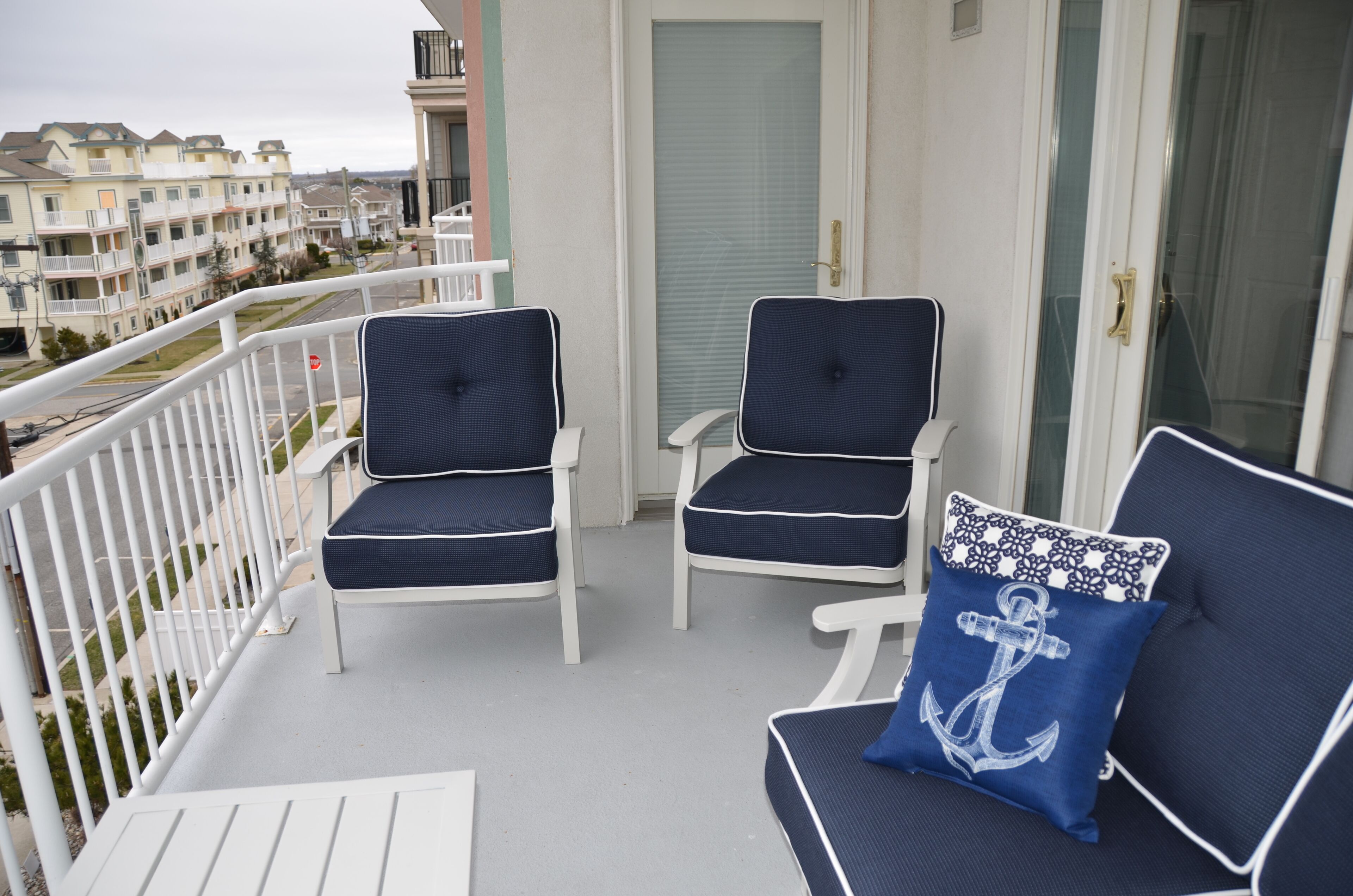 Een balkon met twee witte stoelen en een blauw kussen met een anker dessin.