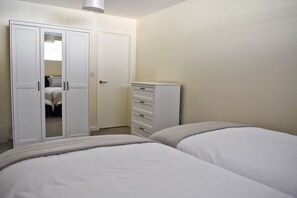 Two beds with white bedding, a wardrobe, and a bedside table with drawers.