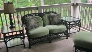 A covered porch with a green cushioned sofa, a small table, and a chair.