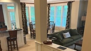 A living room with a green sofa, a coffee table, and a dining area with chairs and a table.