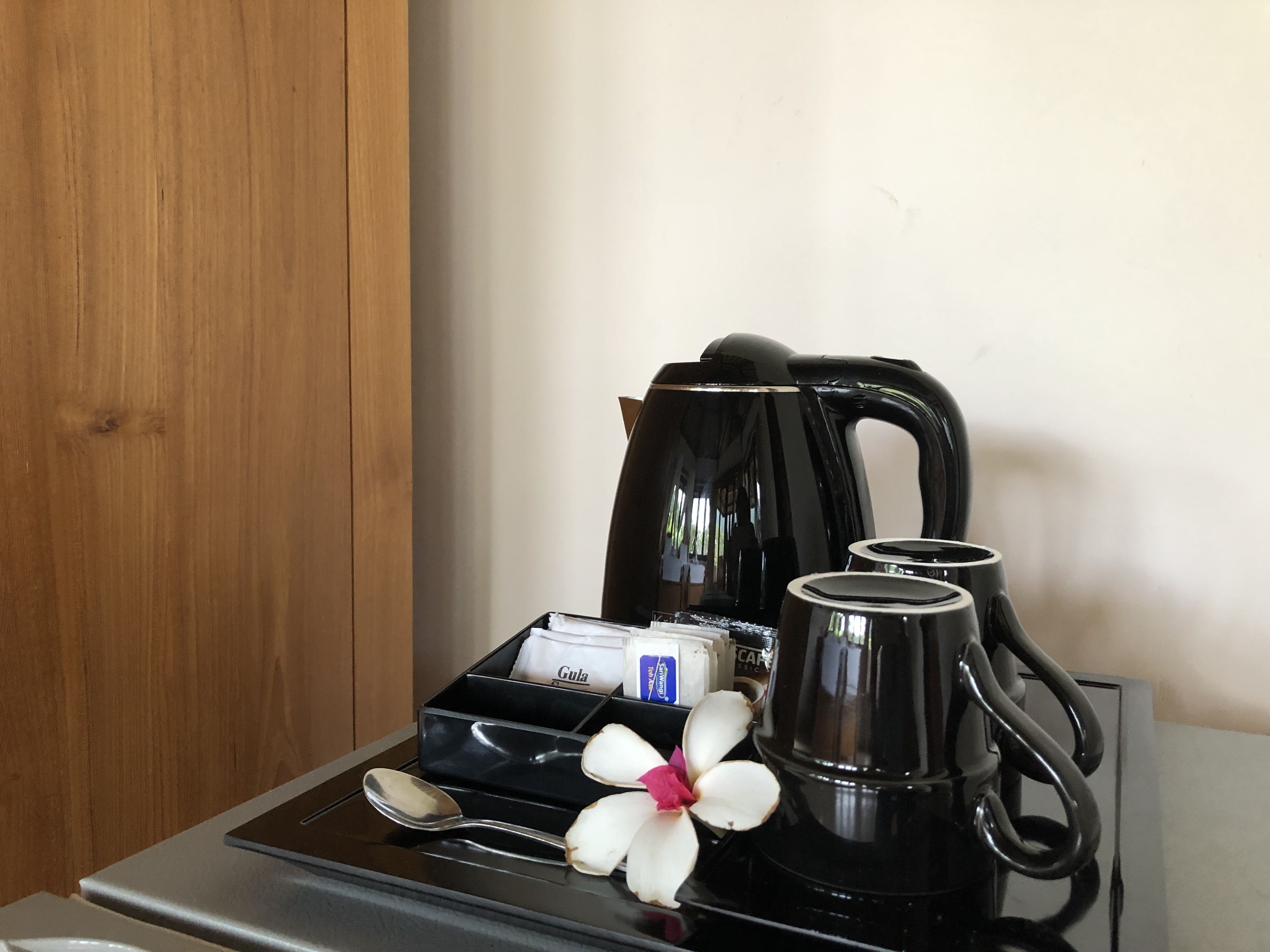 A coffee station with a black coffee maker, two mugs, a spoon, and a small box of sugar.