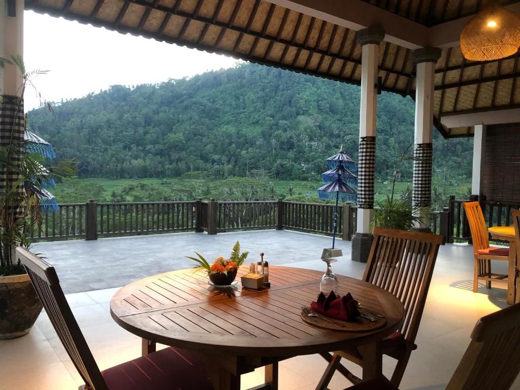 A covered outdoor seating area with a table set for two, overlooking a lush green landscape.
