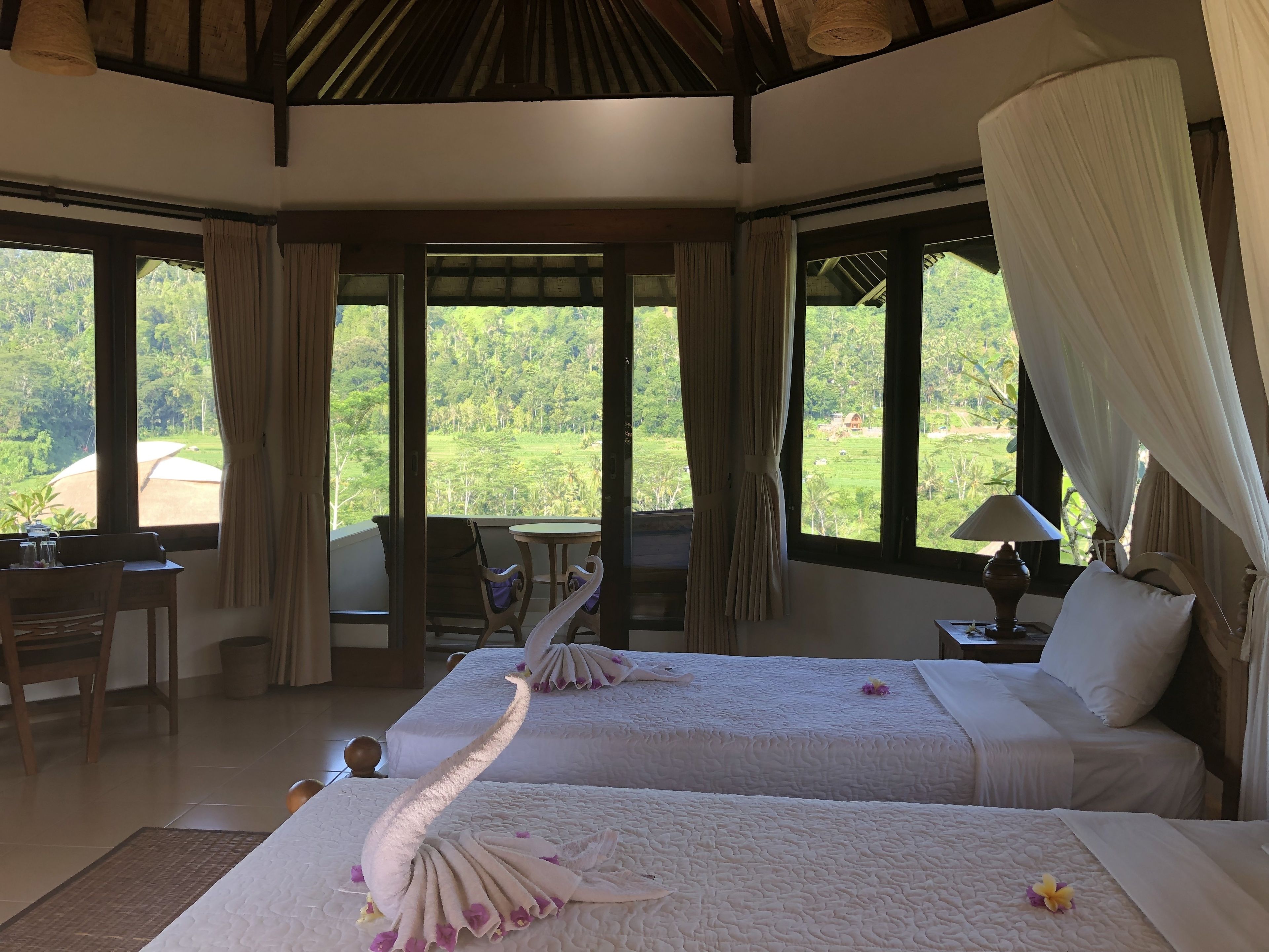 A hotel room with two beds, a dining area, and large windows with curtains.