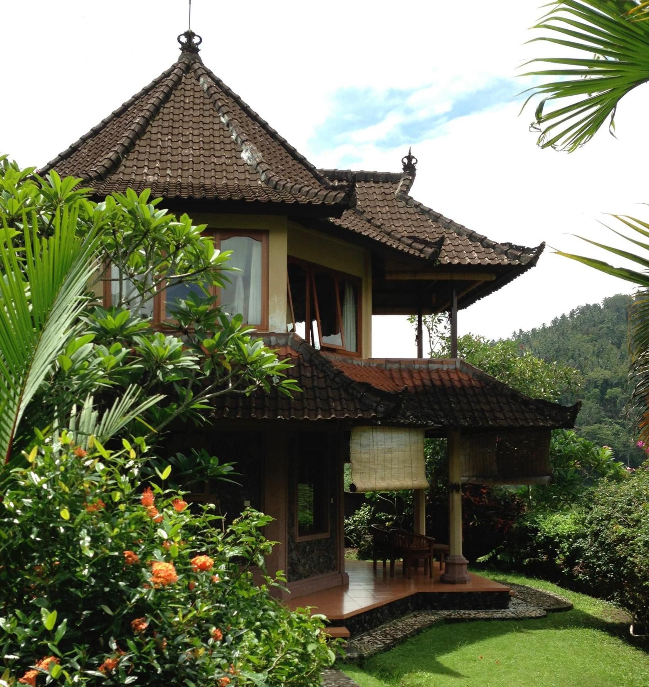 Une maison traditionnelle avec un toit en tuiles, un balcon et un jardin planté de plantes tropicales.