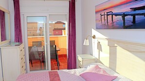 A bedroom with a bed, a desk, a chair, a nightstand, a painting, and a view of the outside. - Apartment close to the beach (TARIFA)