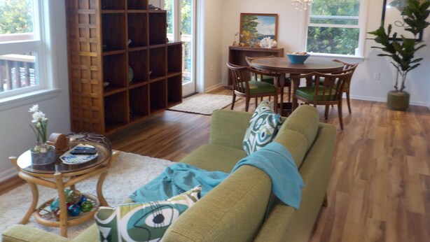 Een woonkamer met een groene bank, een houten boekenkast, een eettafel met stoelen en een kroonluchter.