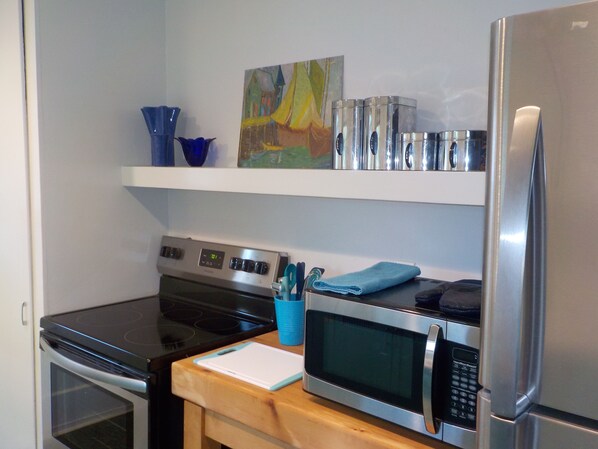 Een keuken met een fornuis, oven, magnetron en koelkast. Op het aanrecht ligt een blauwe handdoek en er hangt een schilderij aan de muur.