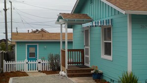 Een turquoise huis met een veranda, een witte hek en het nummer 2670 op de deur.