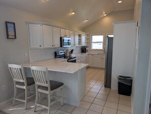 A kitchen with white cabinets, a central island with chairs, a microwave, and a refrigerator.