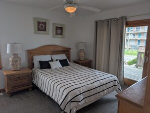 A bedroom with a bed, two nightstands, a ceiling fan, and a view of a balcony.