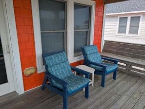 A porch with two blue chairs and a small table, a red wall, and a window with blinds.