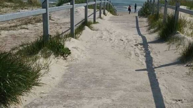 A sandy pathway leading to a beach with a wooden fence on one side.