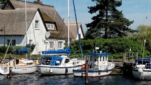 A row of boats docked at a marina with a house in the background.