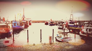Een jachthaven met verschillende boten in de haven, een waterkant met kinderkopjes en een brug op de achtergrond.