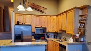 A modern kitchen with wooden cabinets, stainless steel appliances, granite countertops, and a bar area with stools. -    Enjoy the Summer Time in Views!  (Silverthorne)