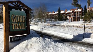 A Gore Trail sign with a contact number, surrounded by snow and buildings in the background. -    Enjoy the Summer Time in Views!  (Silverthorne)