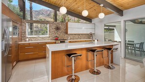 A modern kitchen with a large island, wooden cabinets, and a view of mountains. - Mid-Century Modern Gem - Pool Spa Fire Pit w/ Stunning Views in Vista Las Palmas (Palm Springs)