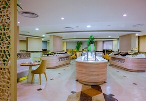 Un moderno vestíbulo de hotel con una recepción central, zonas de estar y un bufé.