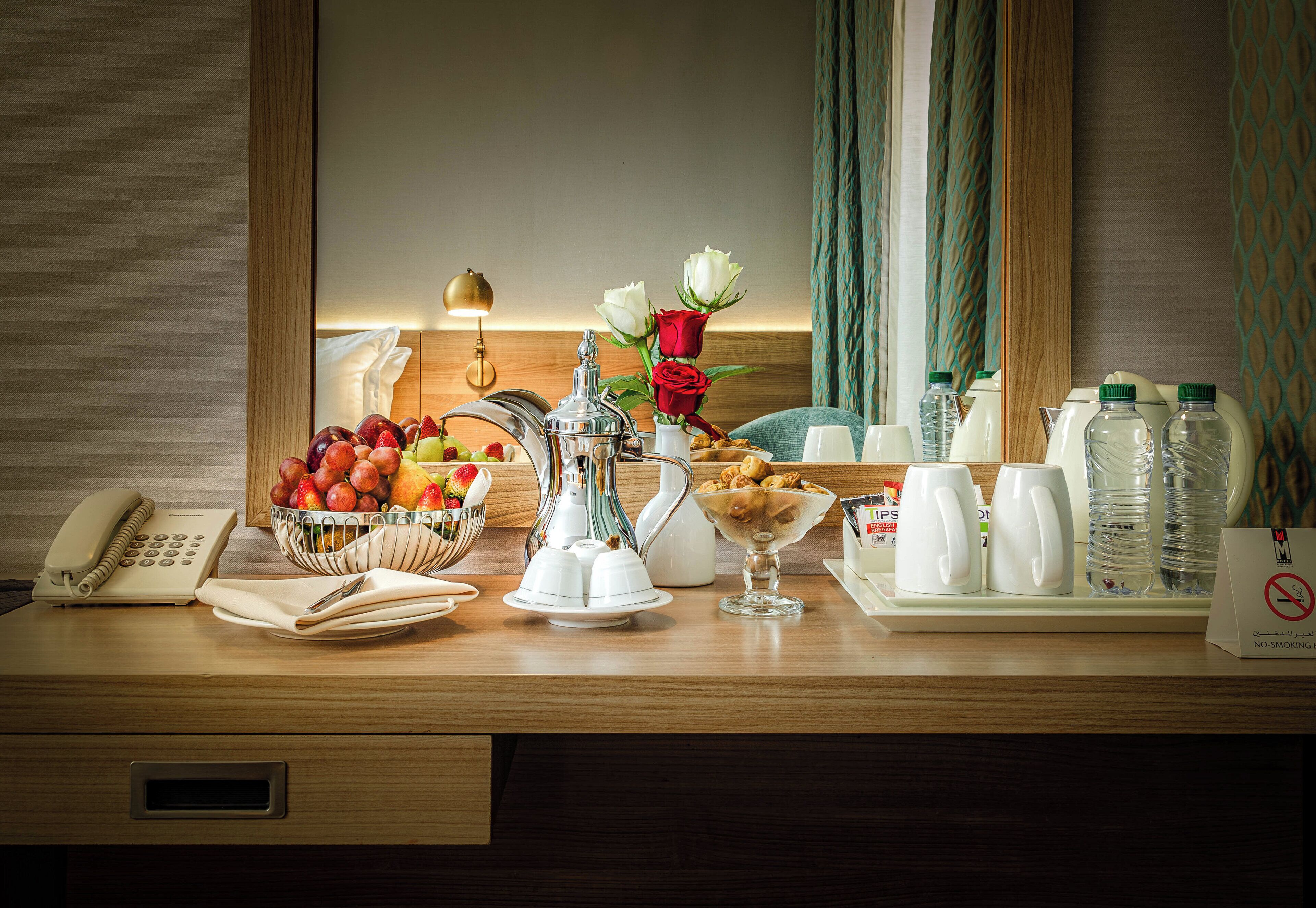 Une table de petit-déjeuner dans une chambre d’hôtel, avec un panier de fruits, une machine à café et un panneau « interdiction de fumer ».
