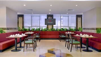 Relax in stylish seating areas with green chairs and tables set with white linens and silverware, surrounded by a geometric tile floor and city views.