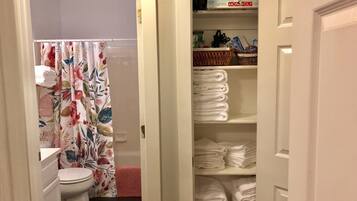 A bathroom with a toilet, a shower curtain with floral patterns, and a storage area with neatly stacked towels.