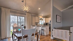Een moderne keuken met witte kasten, een eethoek met een houten tafel en witte stoelen, en een kroonluchter.