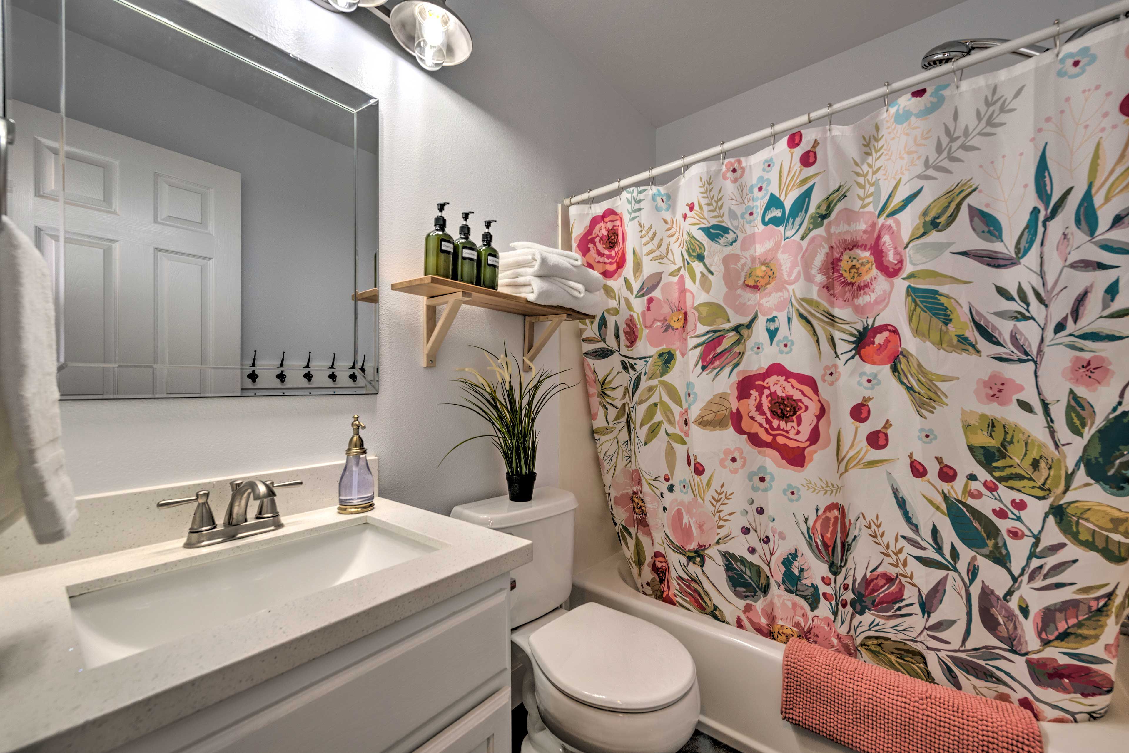 Een badkamer met een wit wastafel, een spiegel, een toilet en een douchegordijn met een bloemmotief.