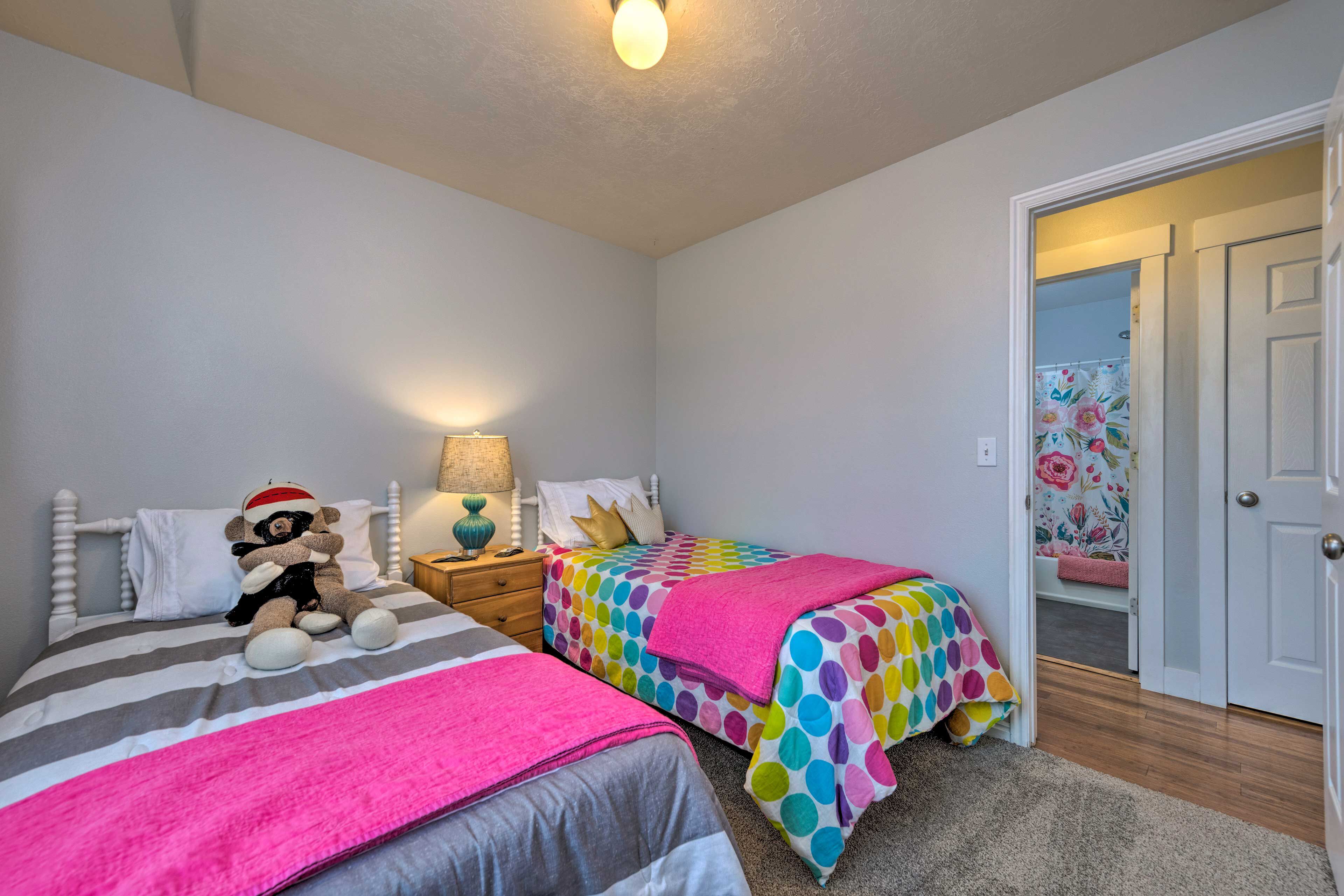 A bedroom with two beds, a nightstand, a lamp, and a teddy bear on one bed.