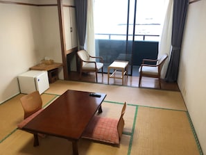 A room with a wooden table, two chairs, a small sofa, a TV, and a mini fridge. - Guesthouse Hamachaya (Minamichita)