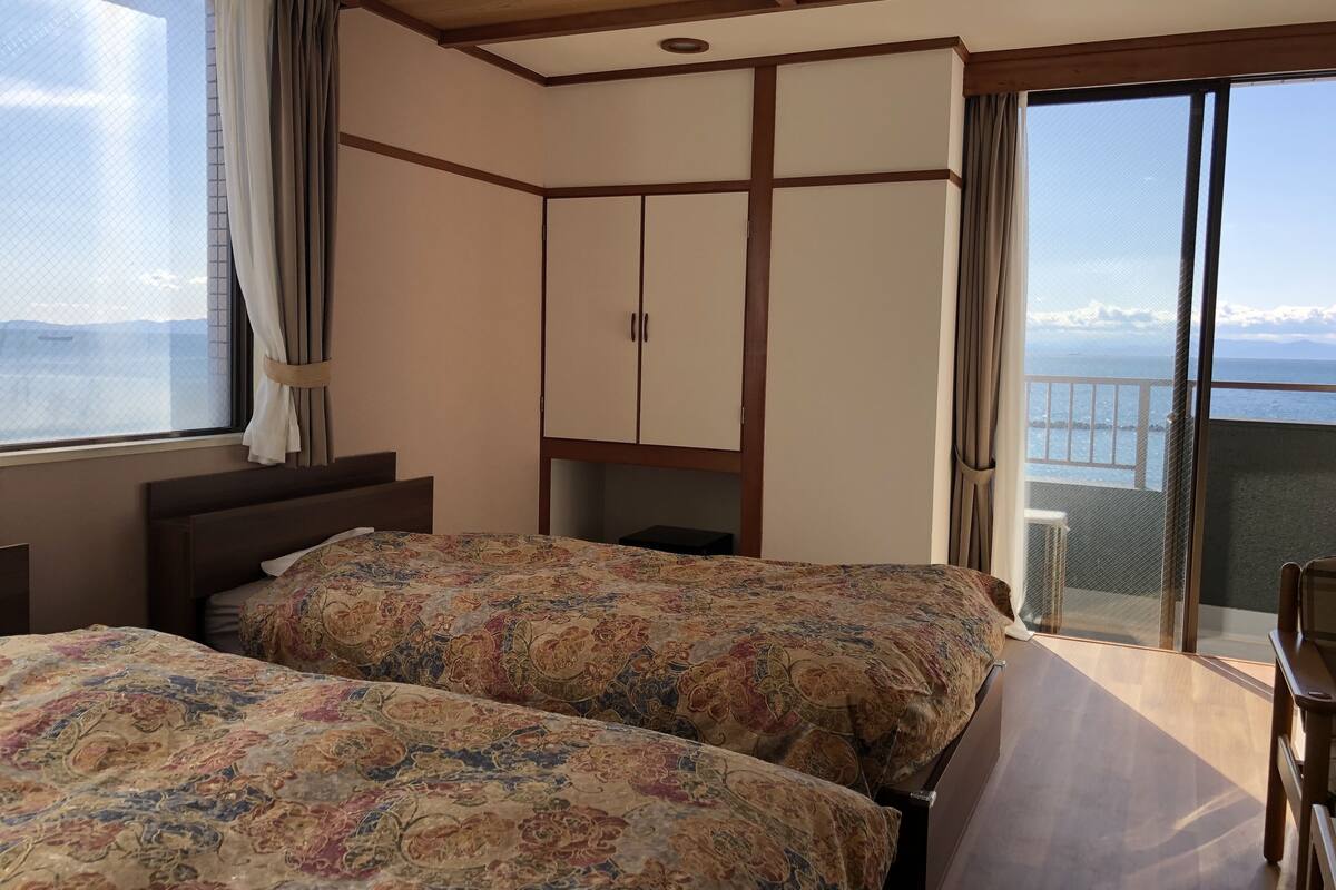 A hotel room with two beds, a wardrobe, and a balcony with a view of the sea.