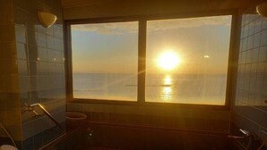 Un baño con bañera, inodoro y ventana con vistas al mar y al sol.