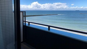 Un balcón con vista al mar, un muelle de madera y un barco a lo lejos.